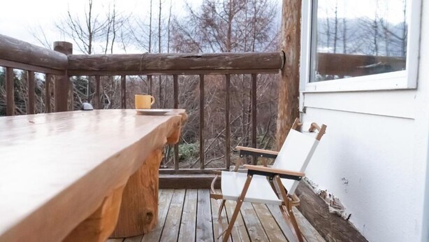 A wooden deck with a table and a folding chair, overlooking a forested area. - Yasunaya (Toyako)