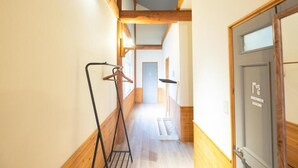 A narrow hallway with wooden beams, a wooden floor, a hanging coat rack, and a door labeled "SHOWER ROOM". - Yasunaya (Toyako)
