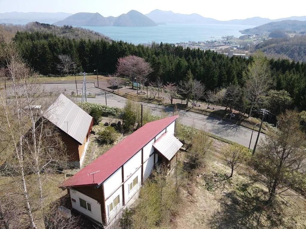 A two-story building with a red roof, surrounded by a parking area and dense forest.