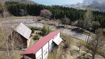 A two-story building with a red roof, surrounded by a parking area and dense forest.