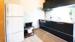 A modern kitchen with a white refrigerator, black cabinets, and a wooden ceiling. - Yasunaya (Toyako)
