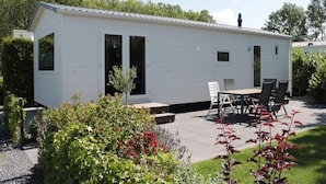 A small, single-story mobile home with a patio area featuring a table and chairs. - Chalet in Friesland Near Wadden Sea & Franeker (Tzummarum)