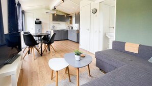 A compact living space with a sofa, dining table, chairs, a TV, and a kitchenette. - Chalet in Friesland Near Wadden Sea & Franeker (Tzummarum)