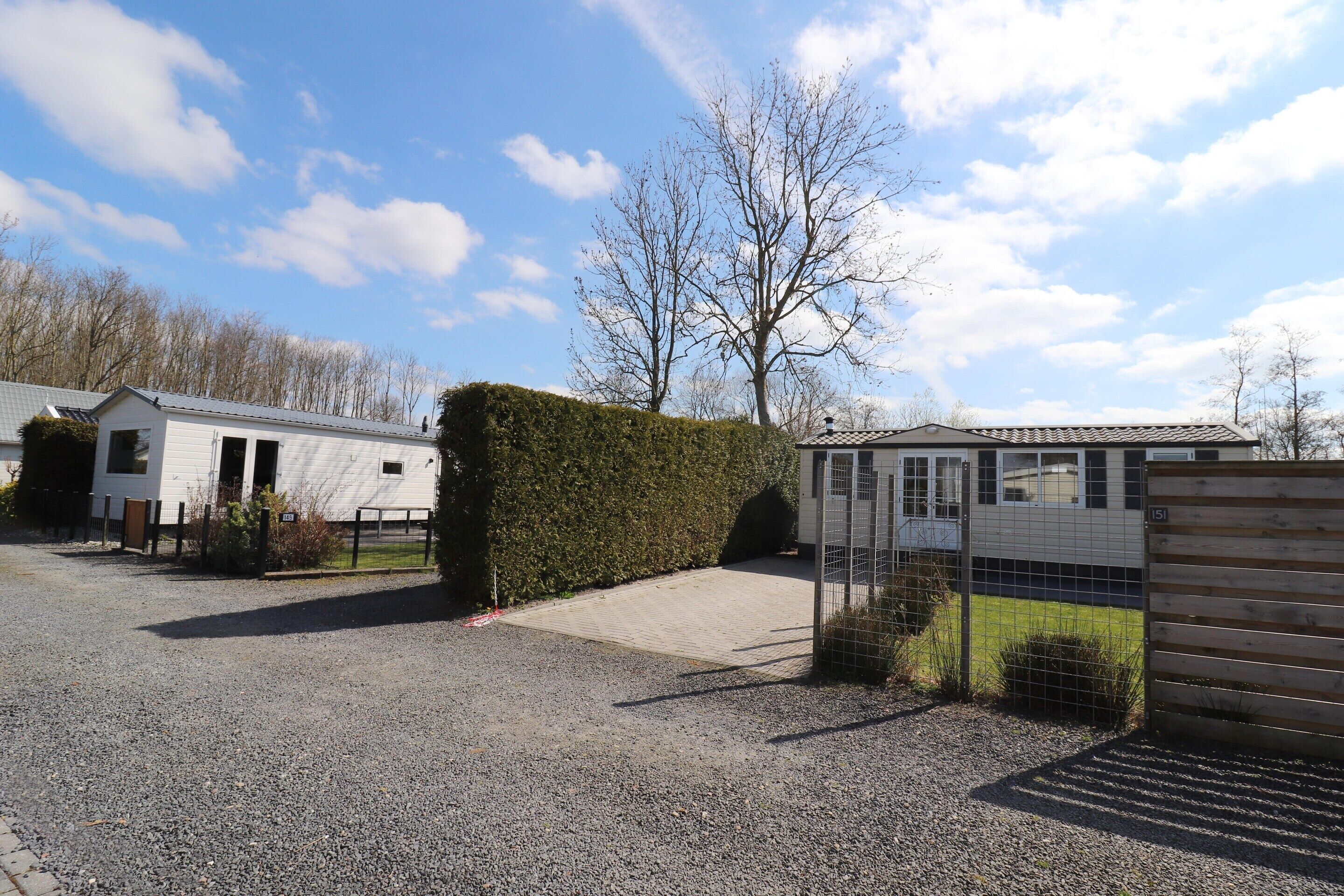 A gravel parking area with a gated entrance, a white building, and a hedge.