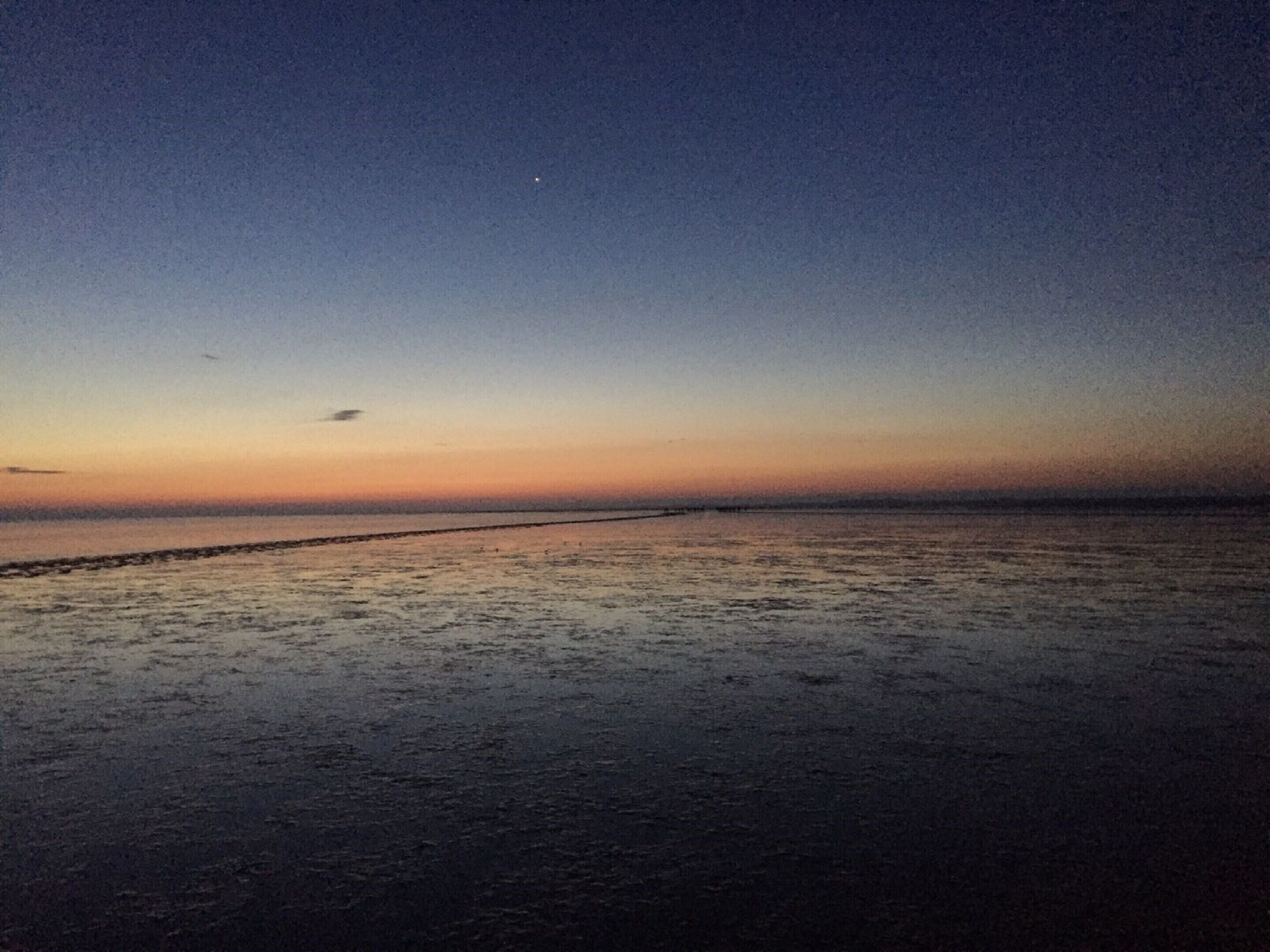A beach at dusk with a calm sea and a clear sky.
