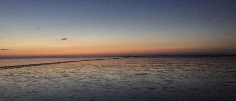 A beach at dusk with a calm sea and a clear sky.