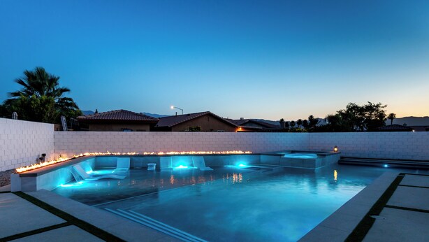 Piscina con asientos y luces integrados, rodeada por un muro de ladrillo y una zona ajardinada con árboles.