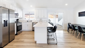 Una cocina moderna con armarios blancos, electrodomésticos de acero inoxidable y una isla central con taburetes de bar.