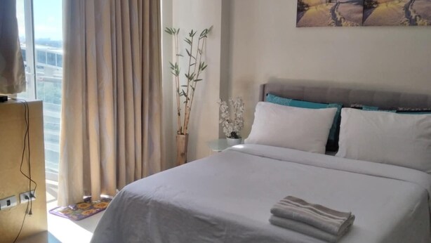 A modern hotel room with a large bed, a view of the city through the window, a painting on the wall, and a small table with a vase of flowers.