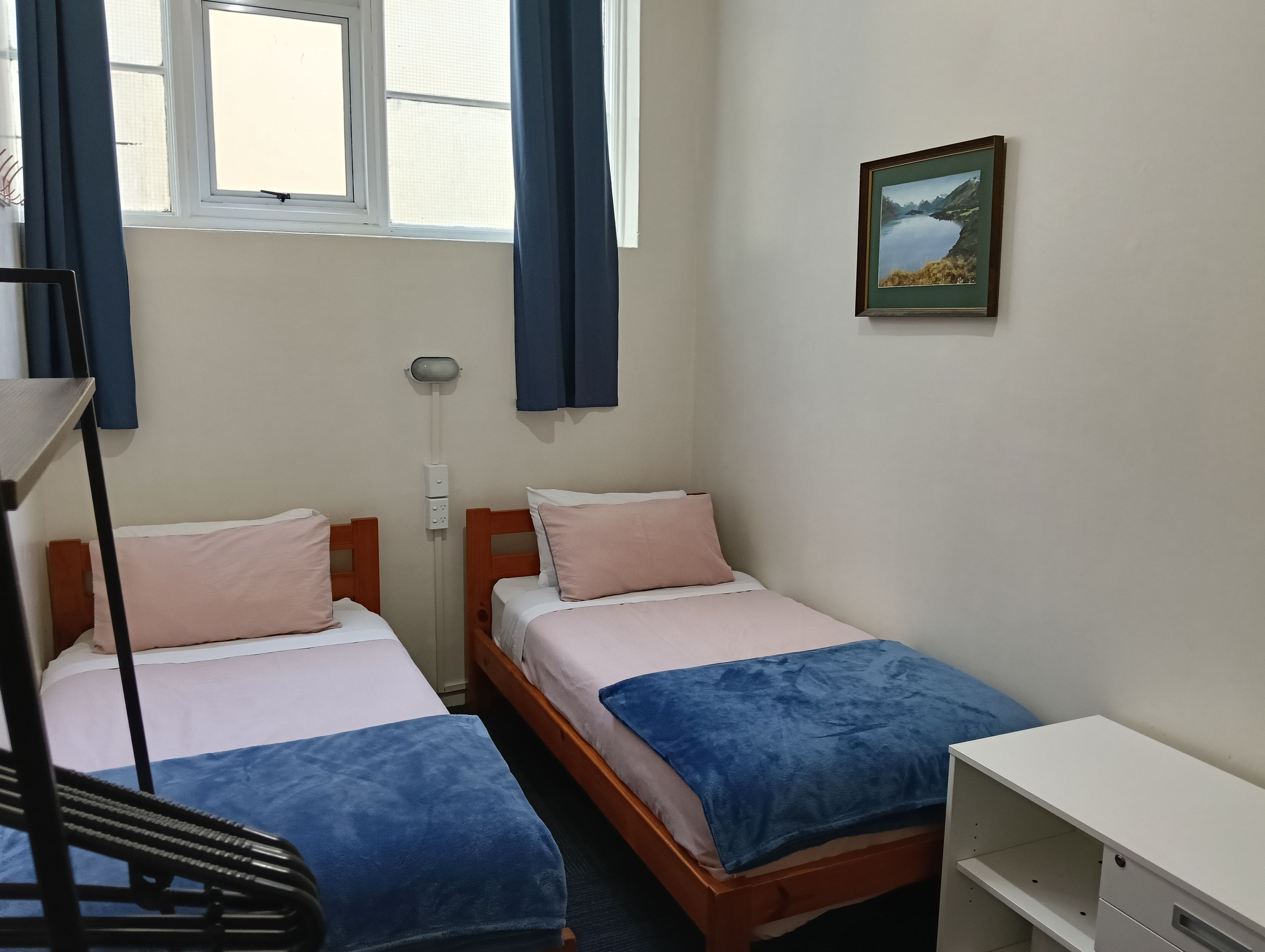 Une chambre avec deux lits, un bureau, une lampe sur pied et une fenêtre avec des rideaux.