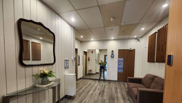 A reception area with a wooden floor, a reception desk with a vase of flowers, a brown sofa, and a mirror on the wall. - Oceanic Hostel (Auckland)