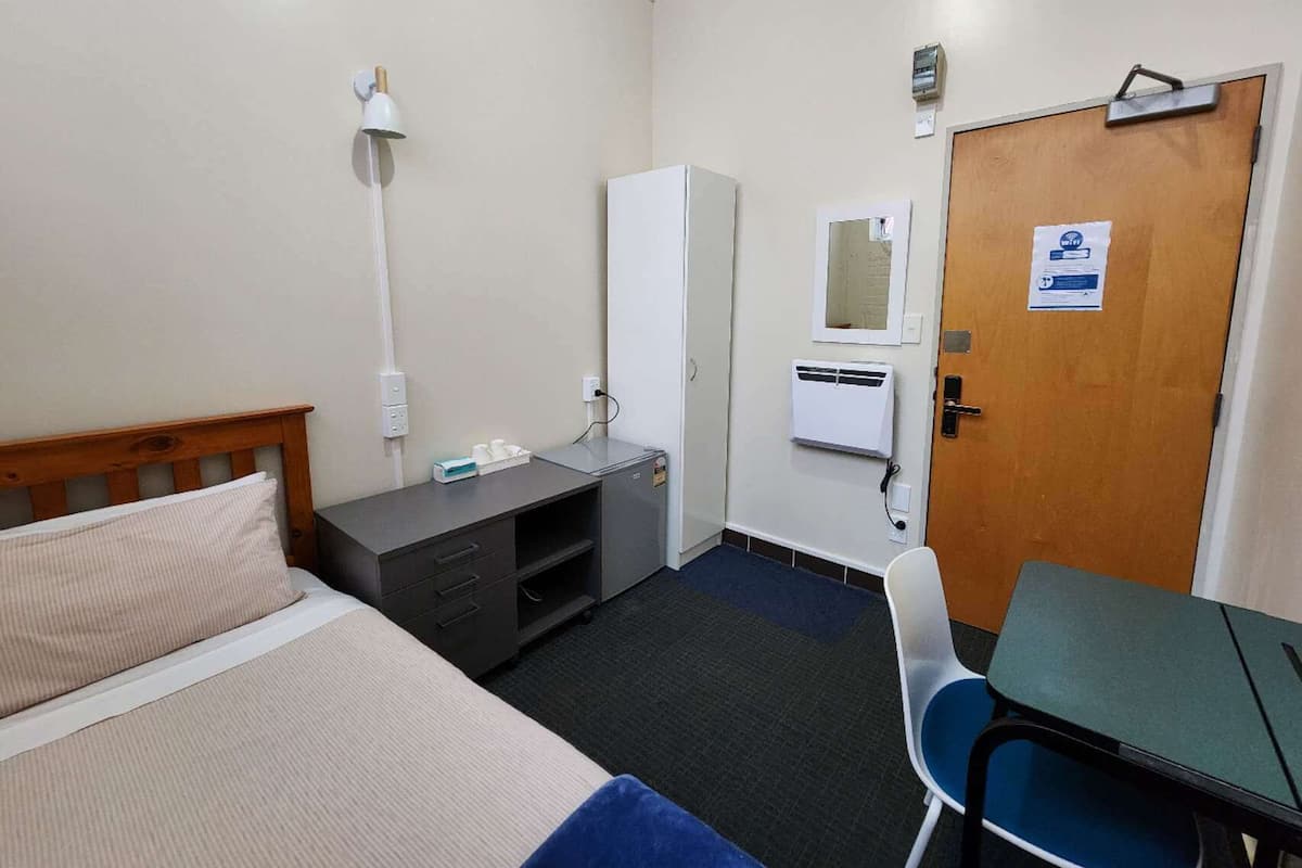 Une chambre d’hôtel comprenant un lit, un bureau, une chaise, une armoire et une porte dotée d’un miroir et d’une pancarte.