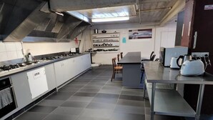 A modern kitchen with stainless steel appliances, a long counter, and a dining area with chairs. - Oceanic Hostel (Auckland)