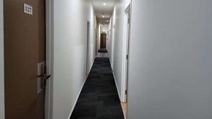 A narrow, well-lit hallway with a black carpet, white walls, and doors on both sides. - Oceanic Hostel (Auckland)