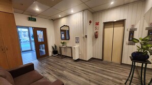 A reception area with a wooden floor, a reception desk, a mirror, a fire extinguisher, and an elevator. - Oceanic Hostel (Auckland)