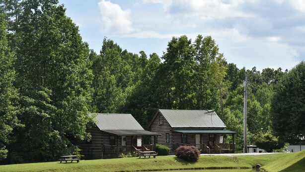 Een rustiek vakantiehuis met een vijver, picknicktafels en een dicht bos op de achtergrond.
