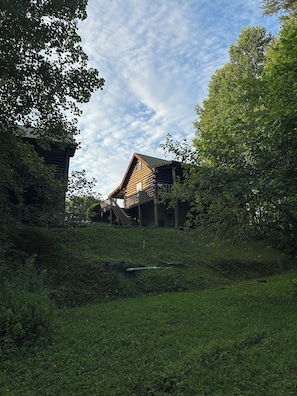 A rustic wooden cabin with a sloped roof, surrounded by lush greenery and a small pond. - Butterfly Nook | Pondside Cabin Near Laurel River Lake & Cumberland Falls (Corbin)