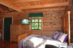 Une chambre dans un chalet en bois, avec un lit, une télévision, une fenêtre et une porte.