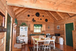 L’intérieur d’un chalet en bois comprend une table à manger, des chaises, un coin cuisine et une porte verte.