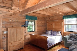 A wooden cabin bedroom with a bed, a chair, a cabinet, and a TV. - Butterfly Nook | Pondside Cabin Near Laurel River Lake & Cumberland Falls (Corbin)