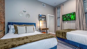 A hotel room with two beds, a TV, a shelf with decorative items, and a brick wall.