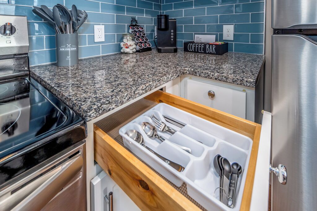 A kitchen with a granite countertop, a coffee bar sign, and a drawer organizer with utensils.