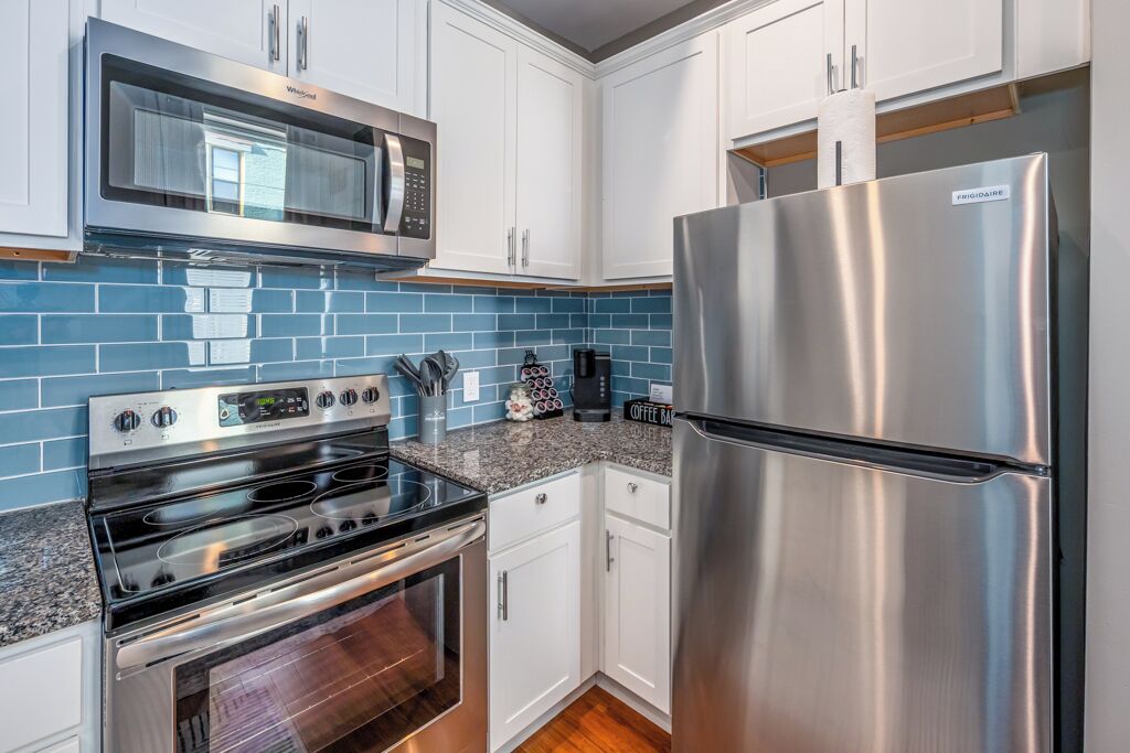 A kitchen with white cabinets, a stainless steel refrigerator, a microwave, and a stove.