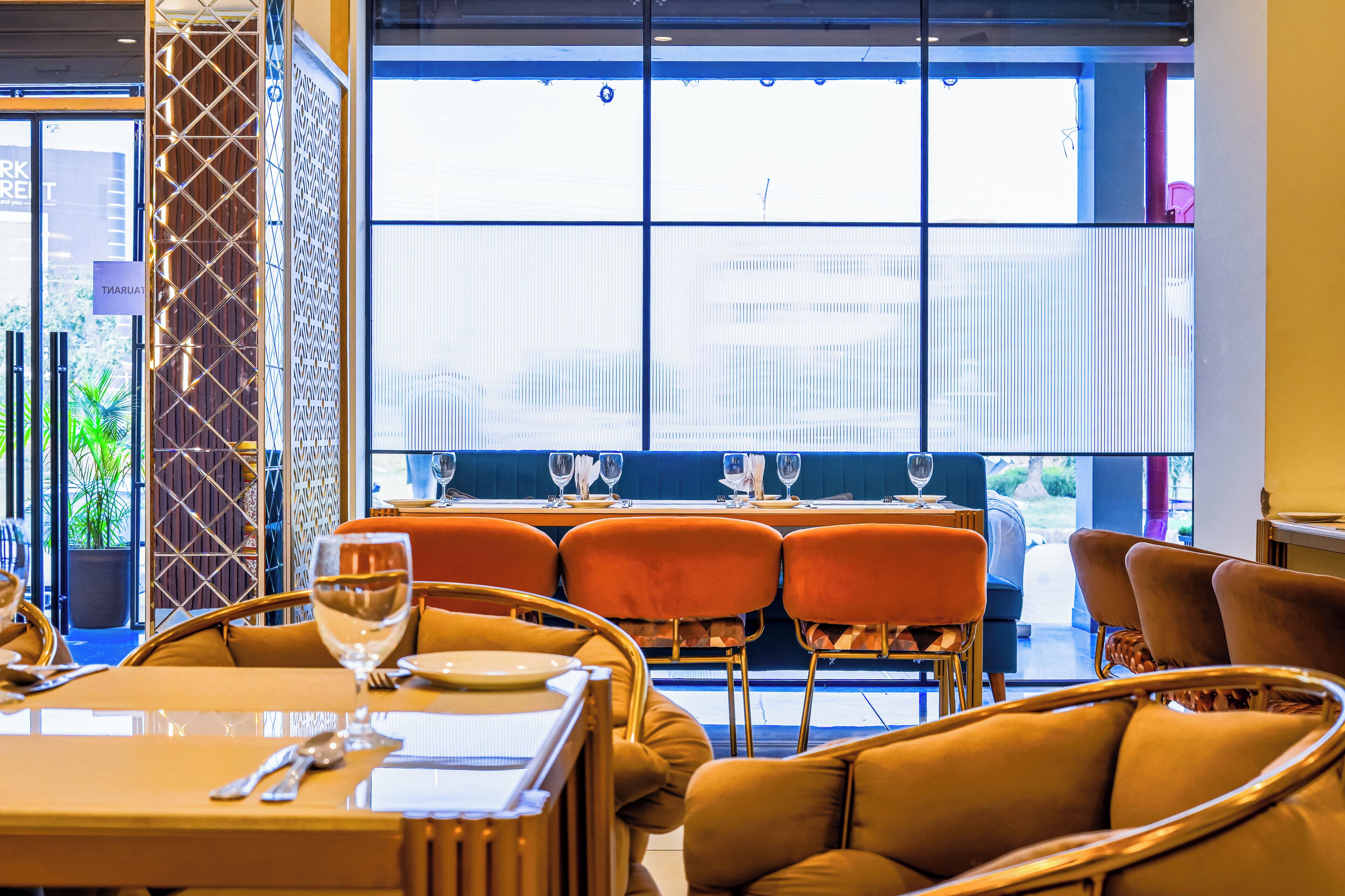 A restaurant with a modern interior, featuring orange seating and a large window with a city view.