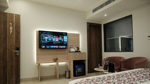 A hotel room with a bed, a desk, a TV mounted on the wall, and a seating area with two chairs. - ACR Luxury Hotel (Mohali)