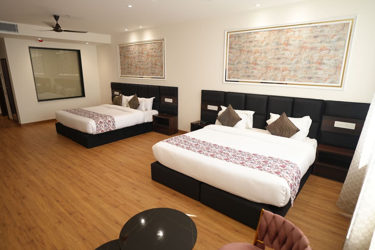 A hotel room with two beds, a ceiling fan, artwork on the walls, and a wooden floor.