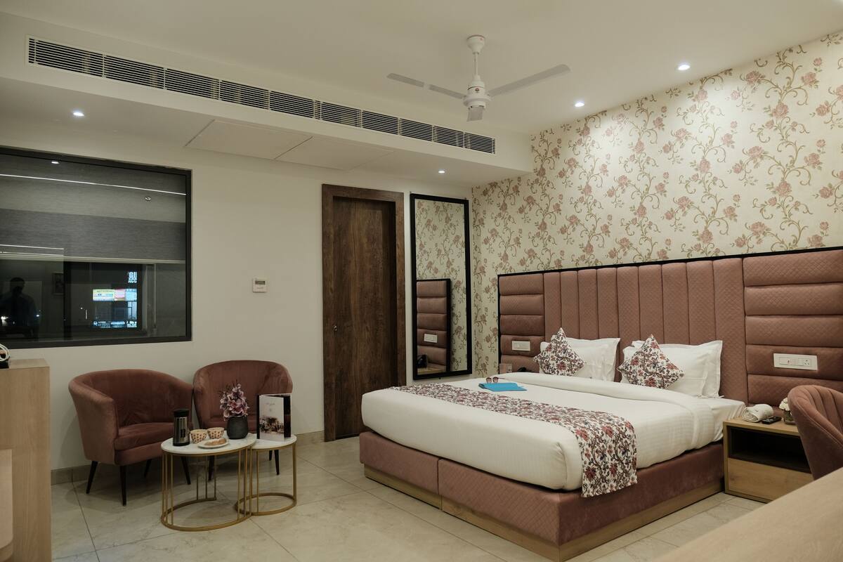 A modern bedroom with a large bed, two armchairs, a small table, and a nightstand.