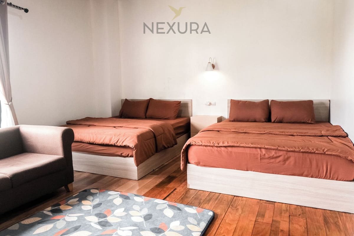 Habitación de hotel con dos camas, una silla, un tapete estampado y una lámpara fijada a la pared.