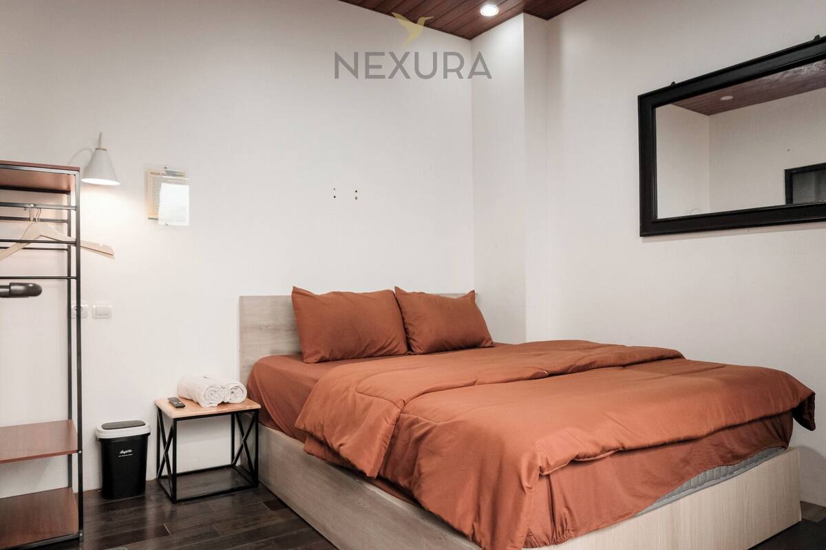 Un dormitorio con cama, mesita de noche, lámpara, espejo y armario.