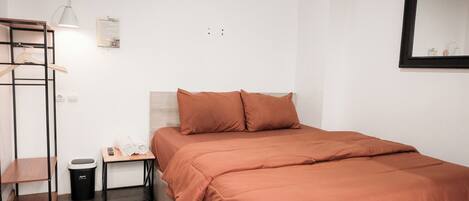 Une chambre d’hôtel bien rangée, avec un lit, un bureau, une chaise, une poubelle et un porte-manteau.