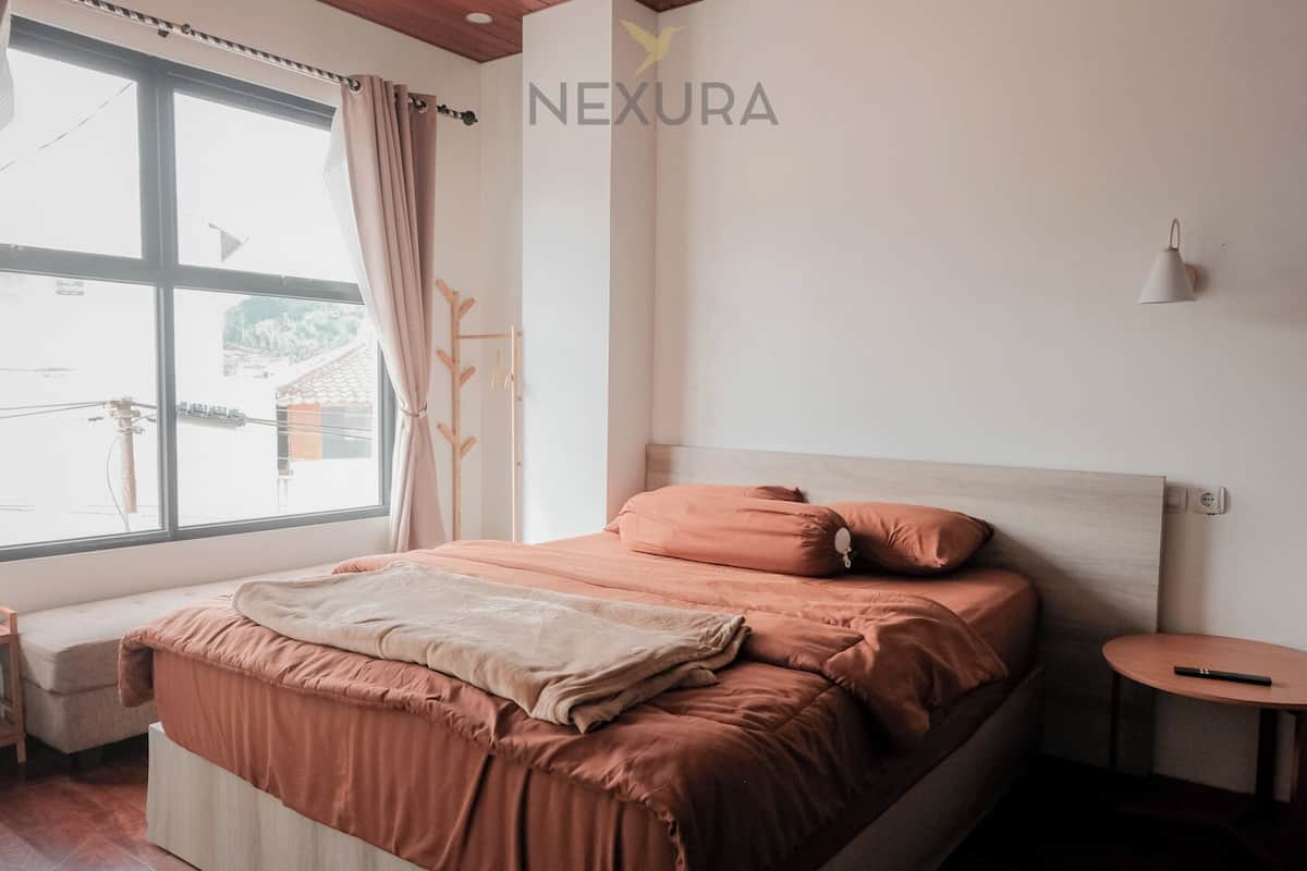 Una cama bien hecha con cabecera, una mesita de noche y una ventana con cortinas.