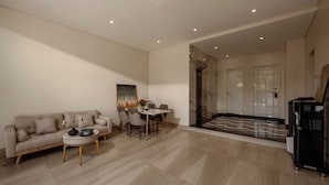 Una sala moderna con sofá, mesa de centro y comedor. Hay un dispensador de agua y una puerta que conduce a otra habitación.