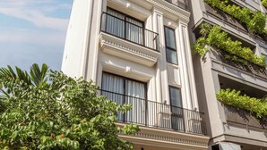 Un edificio de varios pisos con fachada blanca, balcones y un árbol en primer plano.