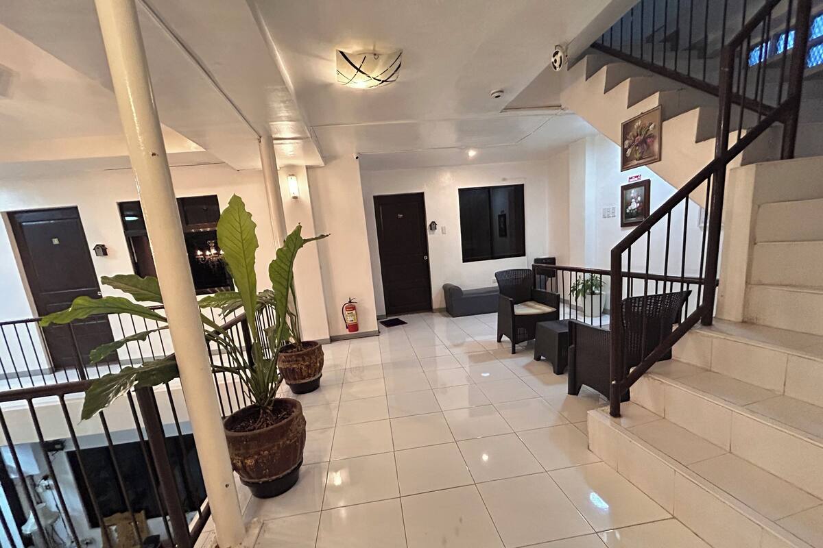 A spacious lobby with a staircase, potted plants, and a fire extinguisher.