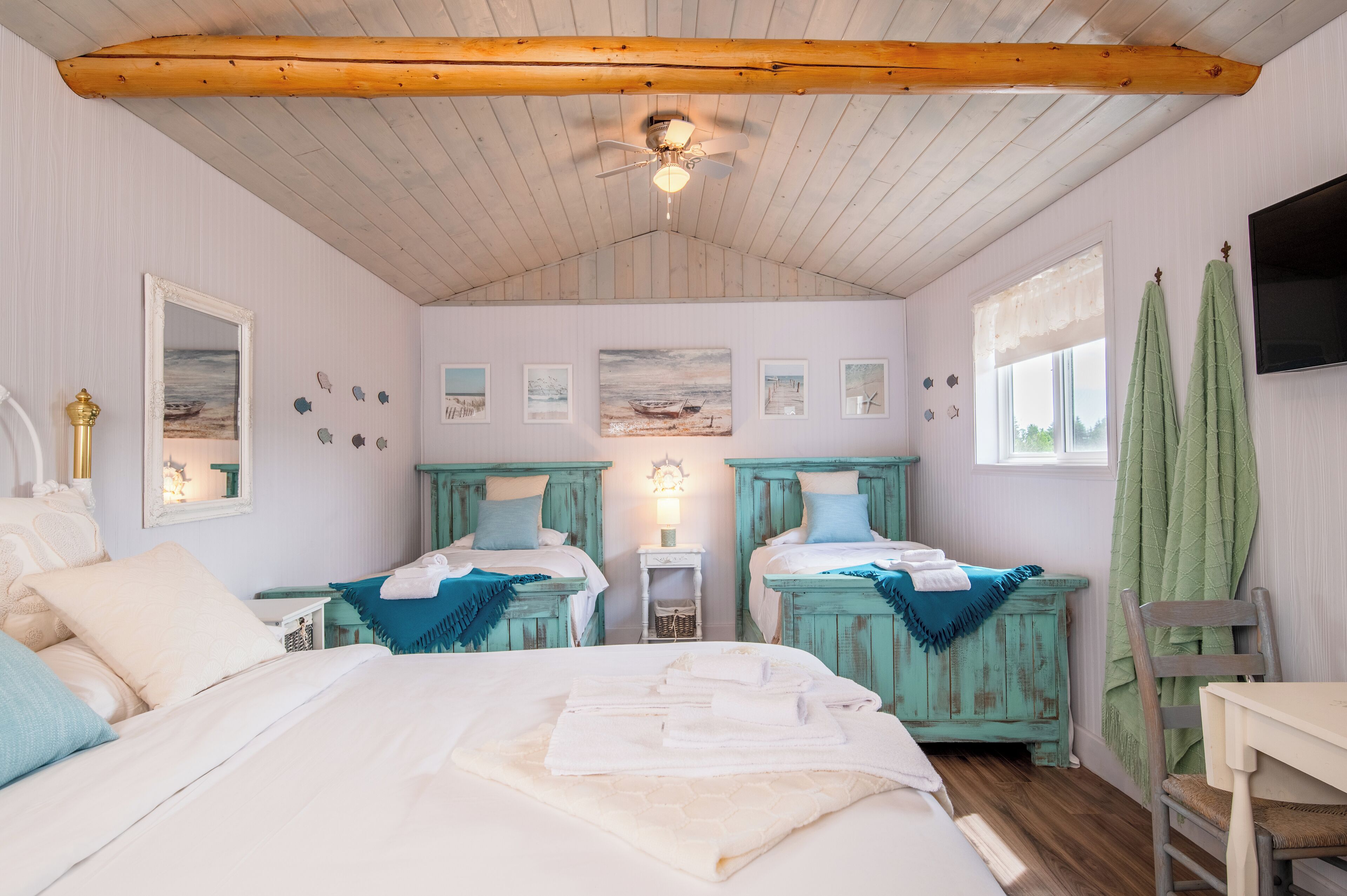 A bedroom with two beds, a wooden ceiling, a TV, and artwork on the walls.