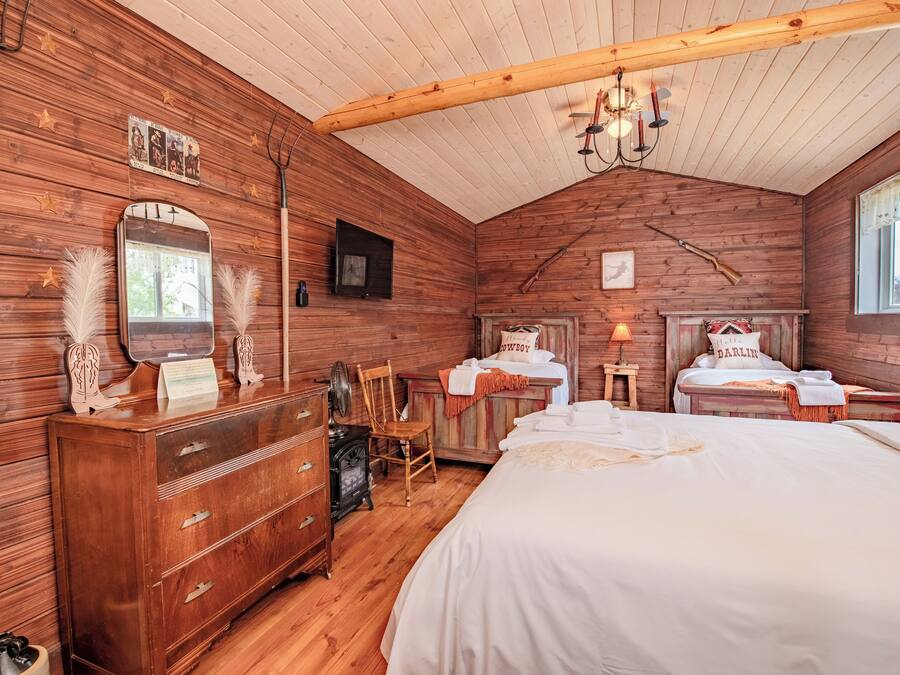 A rustic wooden room with a large bed, a dresser, a chair, and a fireplace.