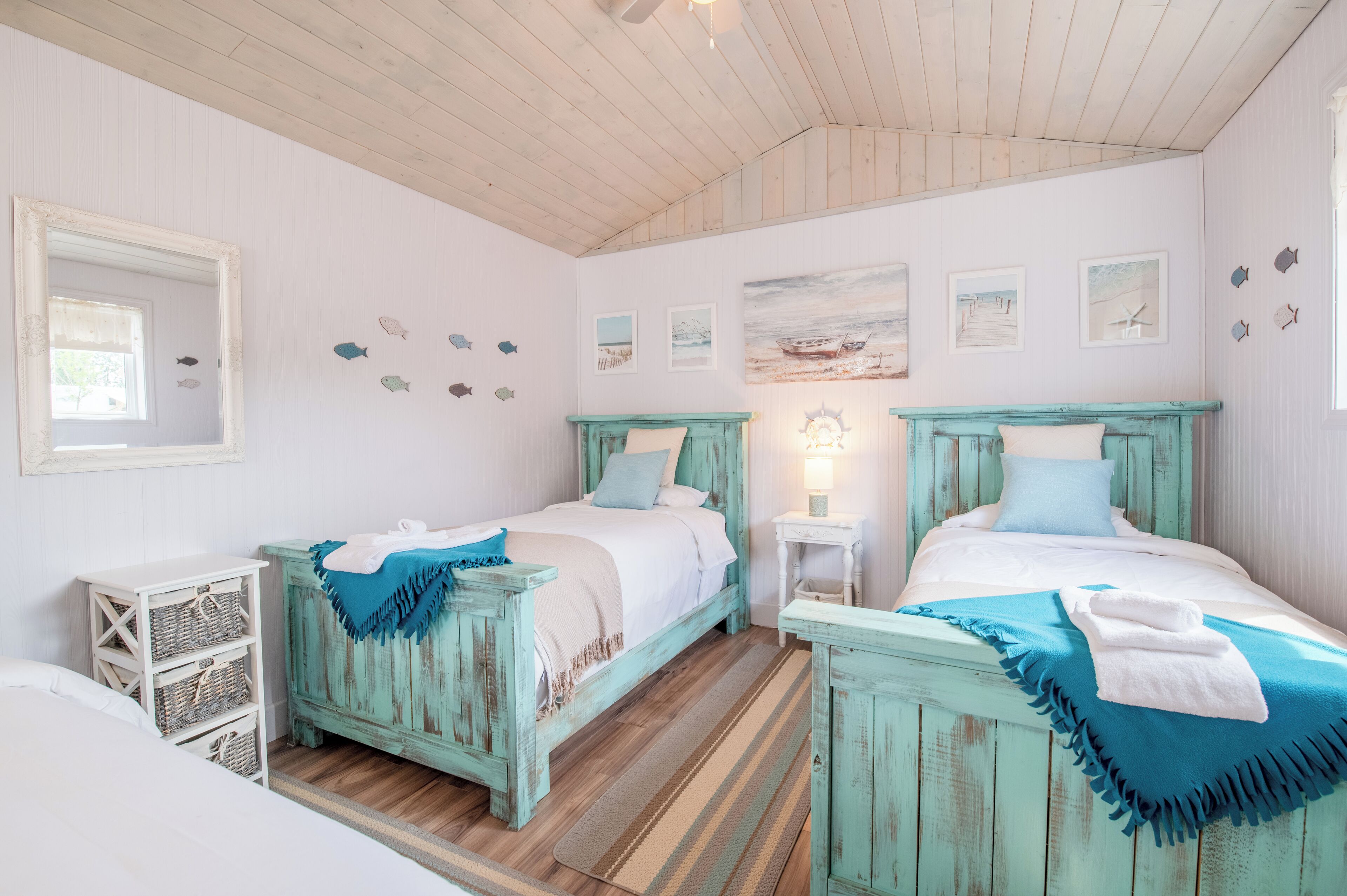 Una habitación con dos camas, pisos de madera, un espejo, decoración en la pared y una pequeña mesa con lámpara.