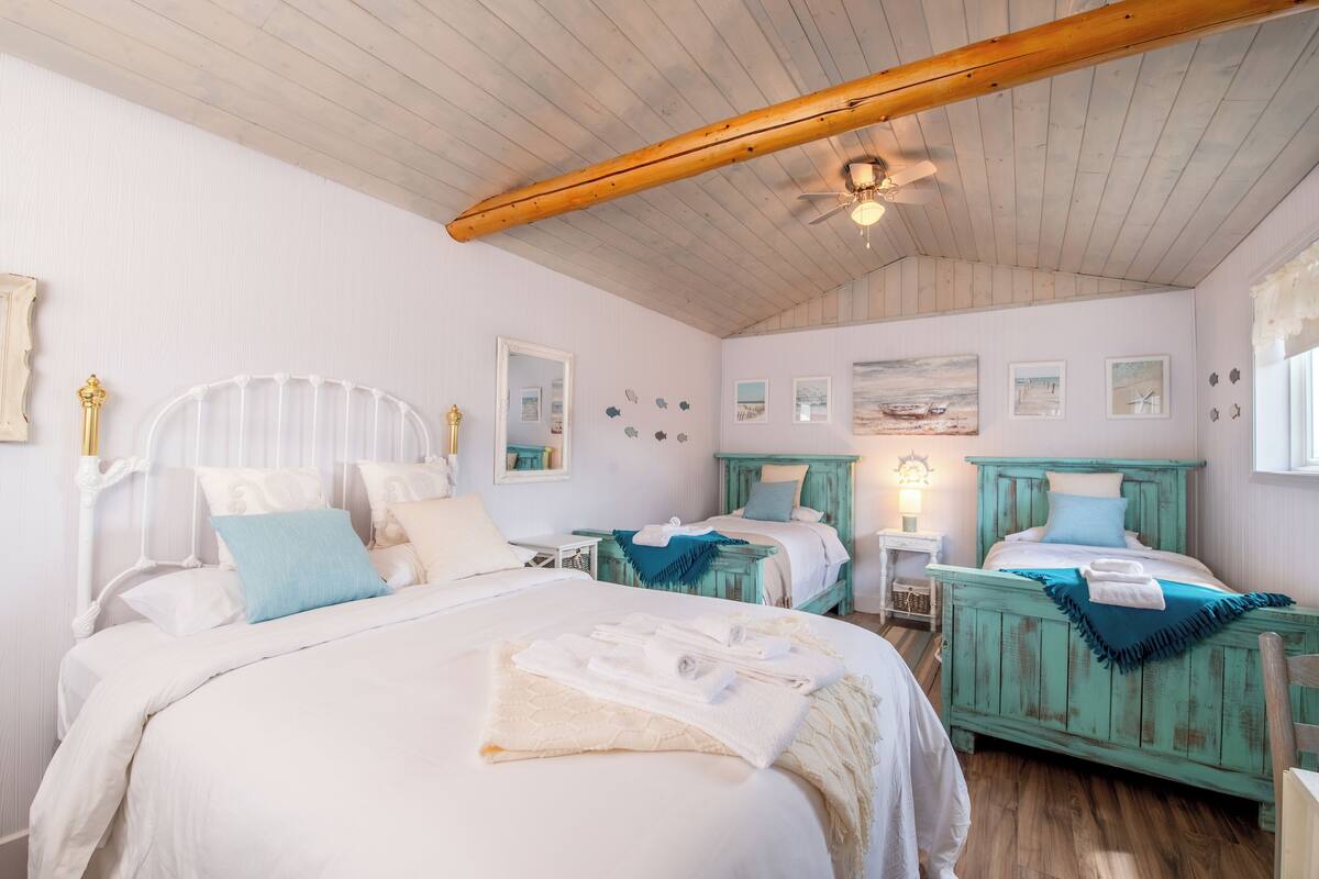 A bedroom with two beds, wooden ceiling beams, and a ceiling fan.