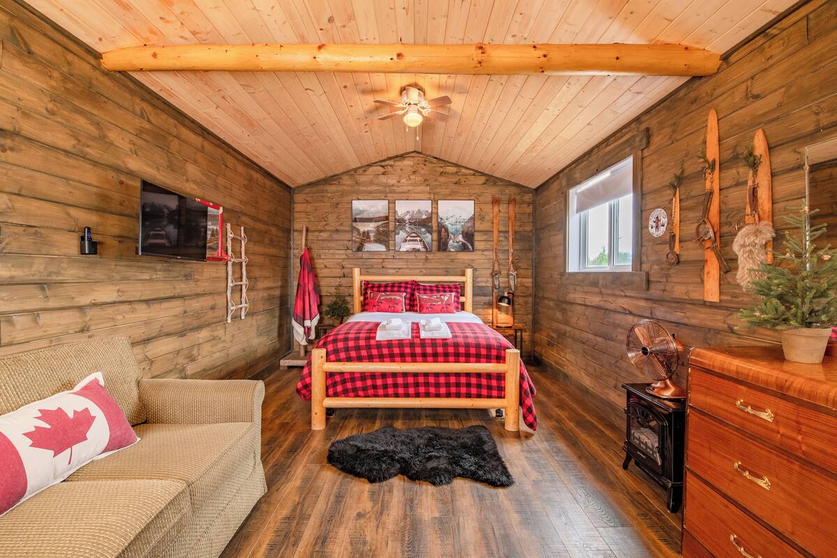 A cozy cabin-style room with a wooden bed, a small sofa, a dresser, and a ceiling fan.
