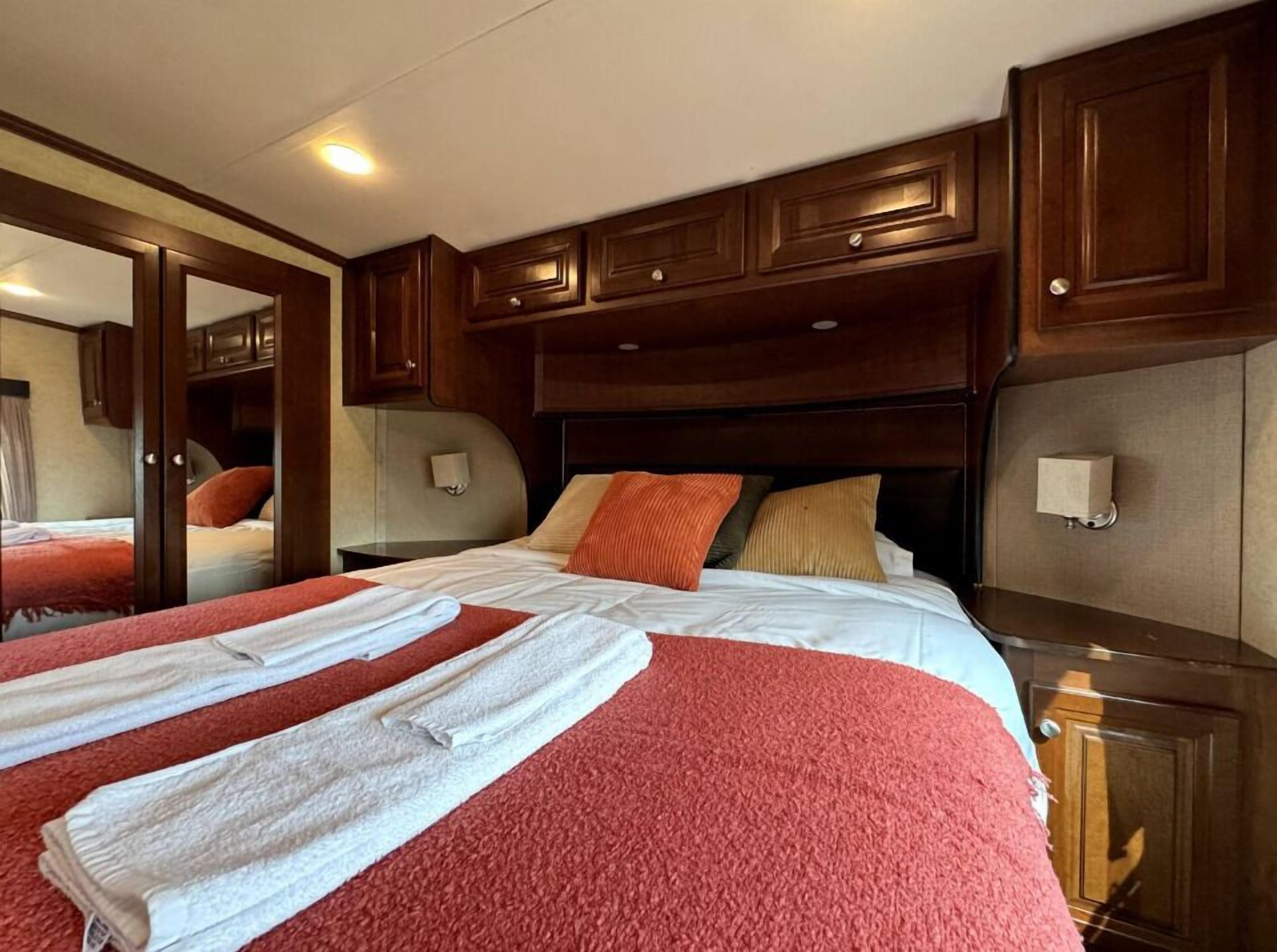 A hotel room with a large bed, wooden headboard, and a mirror cabinet.