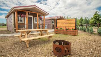 A rustic cabin with a wooden porch, a picnic table, and a fire pit.