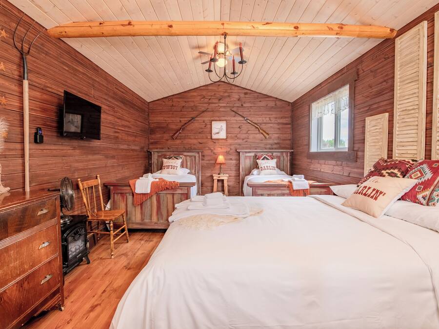A cozy room with a large bed, two bedside tables, a wooden dresser, a vintage stove, and a television on the wall.