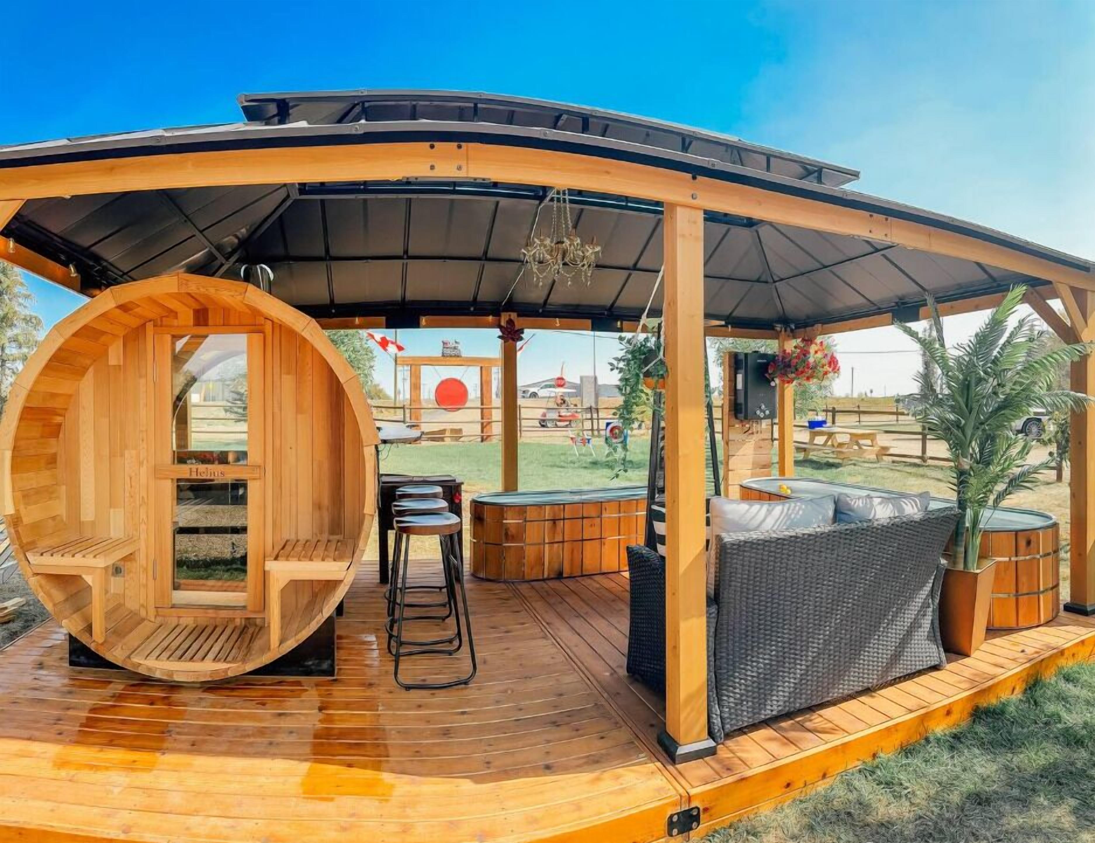 A wooden deck with a sauna, outdoor seating, and a view of a red circular structure in the background.