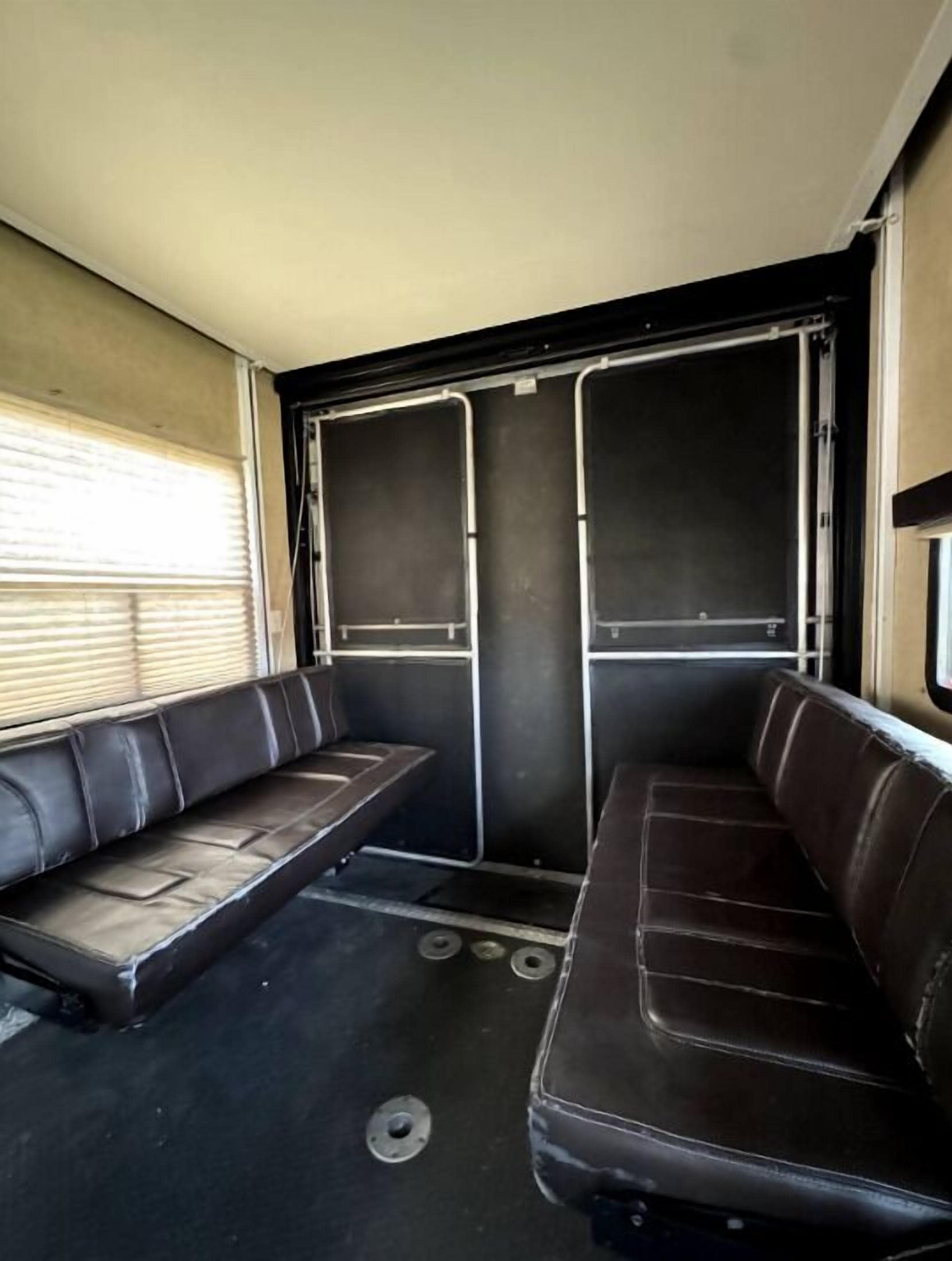 Interior de veículo com dois assentos de couro marrom, uma janela com persianas e uma porta com painéis de metal.