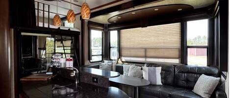 A modern interior with a curved ceiling, a central island with a marble countertop, a black leather sofa, and pendant lighting.