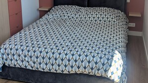 Une chambre à coucher avec une couvre-lit à motifs, une tête de lit sombre et un luminaire fixé au plafond.